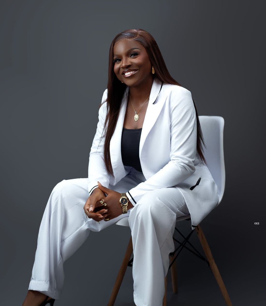 Ayodele Aramide in a white suit, smiling, seated on a white chair